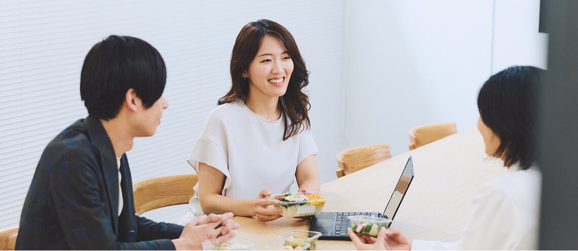 明るいオフィスで和やかに会話する社員3名
