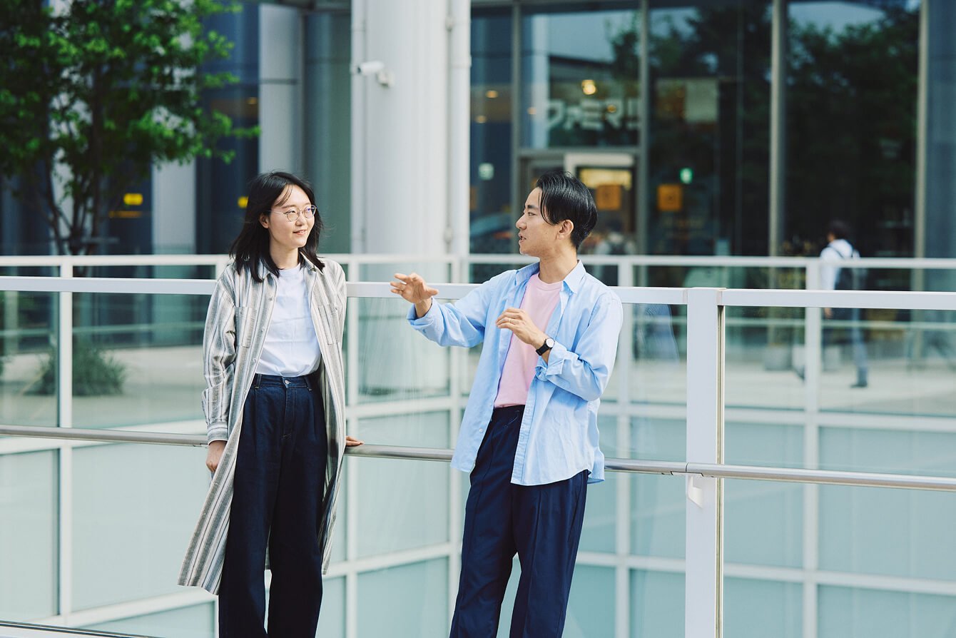 屋外で2人ガラスフェンスにもたれながら話をしている様子