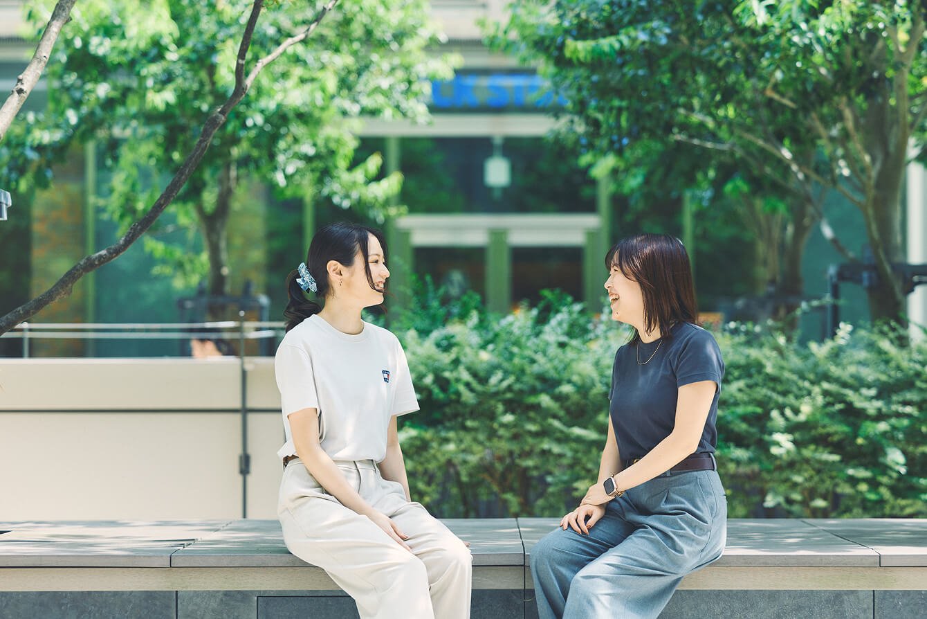 屋外でベンチに座り向き合いながら楽しそうに話している2人