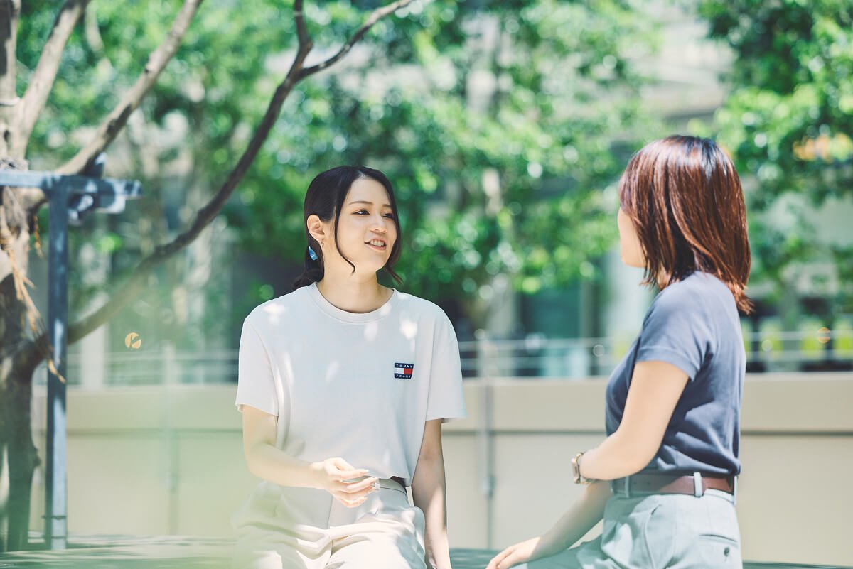 屋外でベンチに座り向き合いながら楽しそうに話している様子の丸田